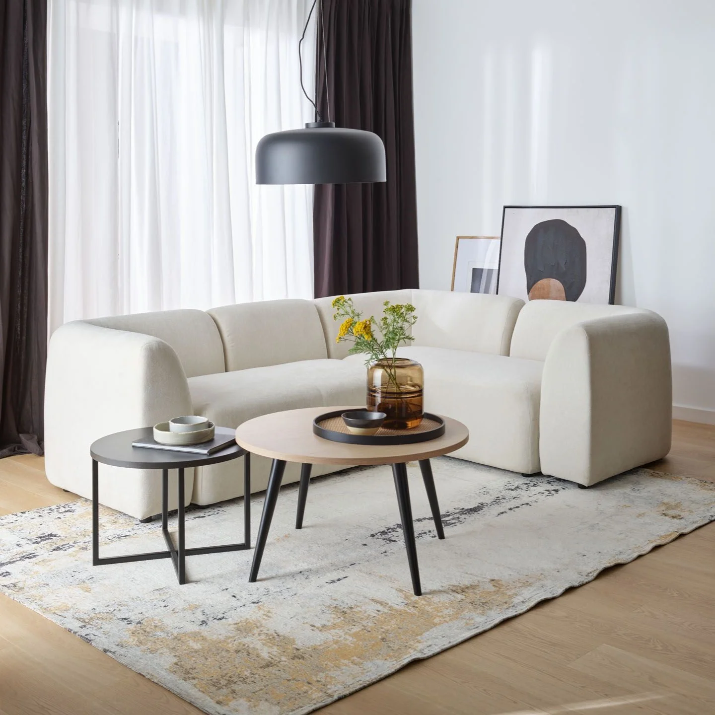 Elegancki salon z jasną sofą i dużą czarną lampą wiszącą nad stolikami kawowymi.